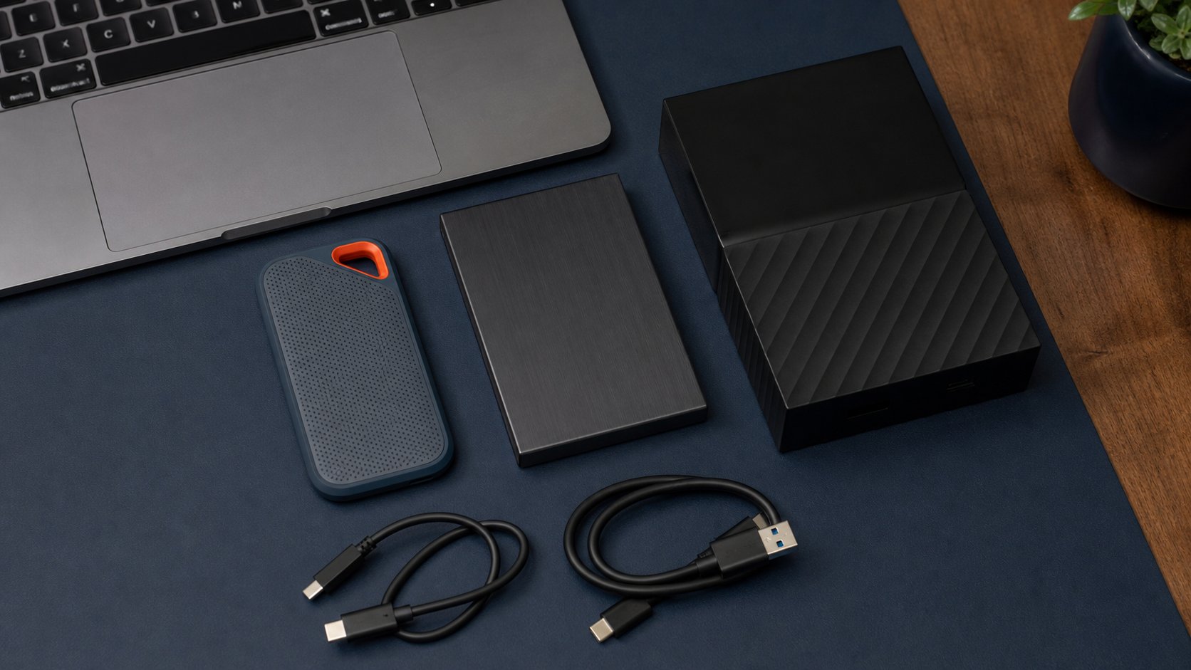 Portable SSD, portable hard drive, desktop backup drive and USB cables arranged beside a laptop